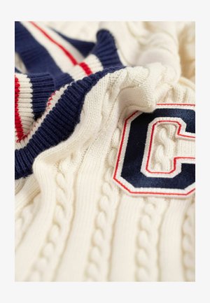 Kabelgebreide trui in crème met navy en rode gestreepte details. Heeft een geborduurd "C"-logo in navy omlijnd met rood. Zachte textuur.