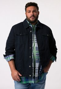 Námořnická denimová bunda přes zelenou košili a kostkovanou flanelovou košili, s knoflíkovým zapínáním, dvěma náprsními kapsami a ohrnutými rukávy.