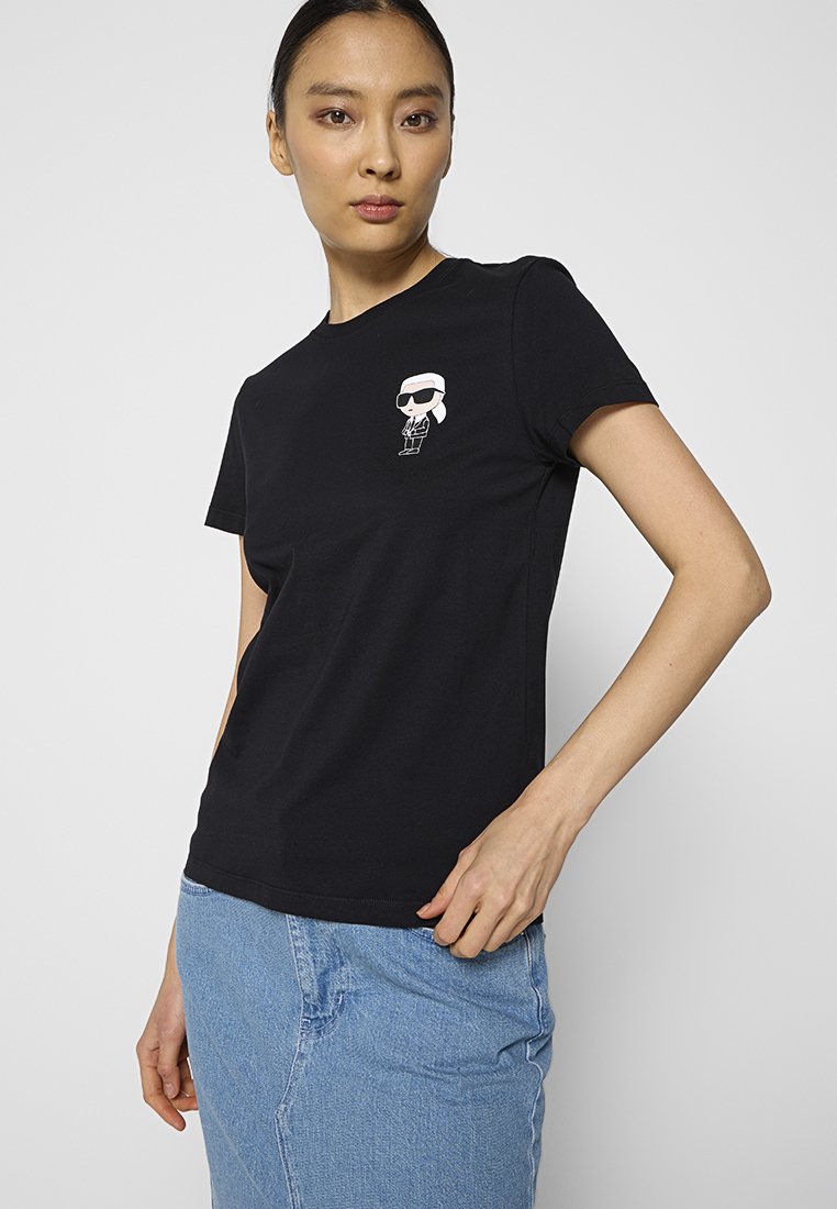 Schwarzes Baumwoll-T-Shirt mit einem kleinen weißen Cartoon-Graphic auf der Brust. Kurzärmlig und mit klassischem Rundhalsausschnitt.