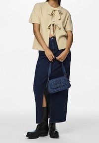 Beżowy sweter z krótkim rękawem z przodu zawiązywany na węzeł, w połączeniu z ciemną jeansową spódnicą z bocznym rozcięciem. Czarne botki na kostkę i torebka z ćwiekami.