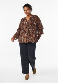 Brown snake-print blouse with a V-neck, featuring ruffled sleeves. Paired with black, loose-fit pants and brown flat shoes.