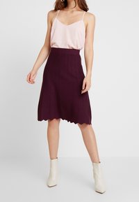 Jupe violette à côtes avec un ourlet festonné, associée à un débardeur rose clair. Des bottines blanches à la cheville complètent la tenue.