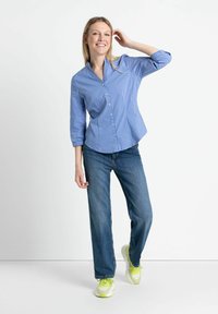 Blau gestreiftes Hemd mit Knopfverschluss in lässiger Passform, kombiniert mit hellblauen Jeans und leuchtend gelben Sneakers. Glattes Material, lange Ärmel.