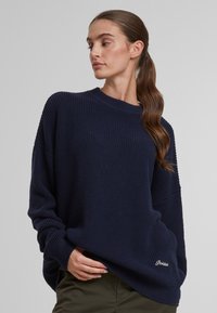 Maglione lavorato a maglia blu navy con texture a coste, vestibilità ampia e spalle dropped. Presenta un sottile dettaglio del logo sull'orlo.