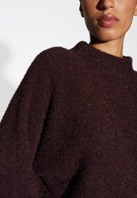 Pull bourgogne avec une finition texturée, présentant un col haut et une coupe ample. Des accents de scintillement subtil ajoutent un intérêt visuel.