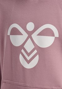 Tessuto rosa con un grande design grafico bianco di una forma simmetrica che somiglia a un ape stilizzata con ali curve ed elementi geometrici.