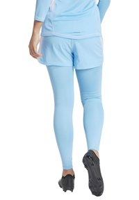 Lichtblauwe sportoutfit bestaande uit een langemouwen top en aansluitende leggings. De stof lijkt glad, met een ademend textuur. Zwarte sport schoenen.