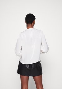 Blusa bianca in satin con maniche lunghe a sbuffo, scollatura rotonda e orlo arrotondato, abbinata a una mini gonna in pelle nera. Tessuto liscio, design minimale.