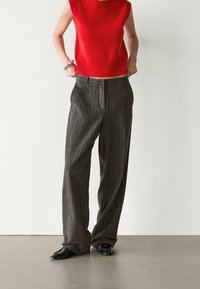 Pull sans manches rouge et pantalon large à rayures grises. Tissu en mélange de laine, lignes verticales, fermeture éclair à l'avant, coupe décontractée. Chaussures noires.