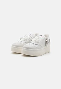 Białe skórzane sneakersy na platformie, z perforowanymi detalami, sznurowanym zapięciem i srebrnym łańcuchem po boku.