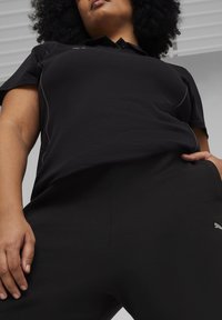 Zwart poloshirt met korte mouwen en een kraag, voorzien van subtiele logo-accenten, gecombineerd met bijpassende zwarte joggingsbroek. Soepele, elastische stof.