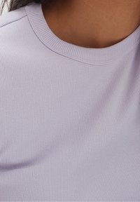 Light lavender ribbed jersey fabric with a smooth texture and a rounded neck. The stitching is subtle and reinforces the edges.