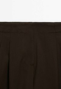 Ruskeat kangashousut, joissa on teksturoitu pinta, edessä laskokset ja huomaamaton takataskusuunnittelu. Sopivat eri tilaisuuksiin.