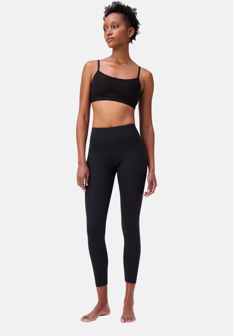 Reggiseno sportivo nero con spalline sottili e fascia con logo; leggings neri a vita alta, taglio aderente, texture liscia, lunghezza alla caviglia.