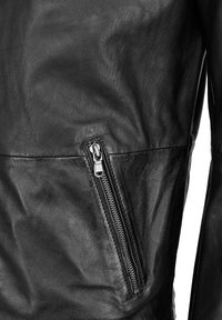 Close-up van een zwarte leren jas met een ritsgebleven schuin zijvak en een gestructureerd leren oppervlak.