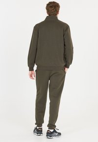 Olive green athletic outfit featuring a zip-up sweatshirt with a high collar and matching joggers. Made of soft fabric with ribbed cuffs.