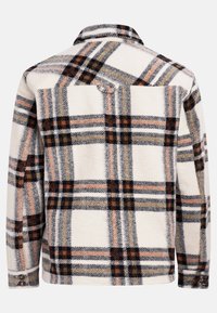 Chemise en flanelle à carreaux beige, avec des motifs en noir, orange et gris. Poignets boutonnés et détail au dos. Tissu doux et texturé.
