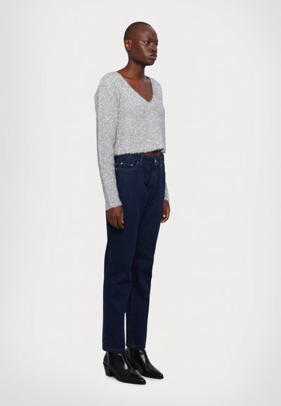 Sølv teksturert crop genser med V-hals, kombinert med mørkeblå jeans og svarte ankelboots, som fremhever en slank og tett silhuett.