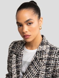 Blazer in tweed bianco e nero con colletto strutturato, indossato sopra una maglietta grafica bianca. Tessuto dalla texture liscia con motivi distintivi.