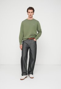 Πράσινη φούτερ με μακριά μανίκια, γκρι παντελόνι φαρδιάς γραμμής, καφέ ζώνη και λευκά αθλητικά παπούτσια. Λεπτό ύφασμα, casual εφαρμογή, μίνιμαλ λογότυπο στο στήθος.