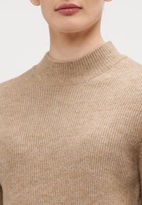Maglione a collo alto beige a coste con un'alta scollatura e una texture morbida, design aderente senza cuciture o motivi visibili.