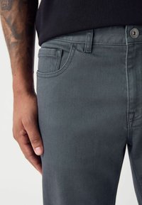 Jeans de denim gris con un ajuste slim, diseño clásico de cinco bolsillos, con cierre frontal de botón y textura suave.