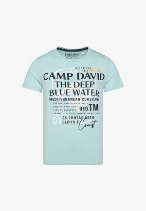 Világoskék, rövid ujjú póló, amelyen merész fekete és fehér szöveg található, grafikai kialakítással és narancssárga kiegészítőkkel. Puha pamut anyag.