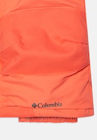 Sekcja kurtki Columbia w jaskrawym koralowym kolorze, wykonana z teksturowanej tkaniny. Posiada logo na dole oraz elastyczny dół dla snug fit.
