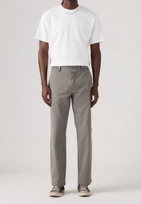 Vit bomullströja, grå denimbyxor, klassisk passform, rak benstil, minimalistisk design, matchad med svarta sneakers och ett silverkedjehalsband.