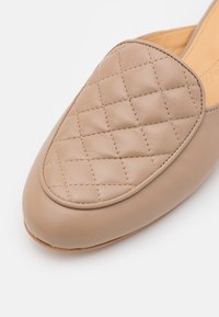 Sapato slip-on em couro bege com textura matelassada na parte superior, bico arredondado e um design liso e minimalista.