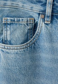 Gros plan sur un jean en denim bleu clair montrant une petite poche à l’intérieur d’une poche avant plus grande avec des coutures orange et un bouton en métal.