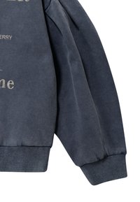 Sudadera gris oscuro con una textura suave, con dobladillo y puños acanalados, y letras bordadas en la parte frontal. Detalle de la manga mostrado.