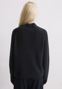 Pull noir à côtes avec un col haut et des manches raglan, dotée d'une finition texturée et d'une coupe décontractée à l'arrière.