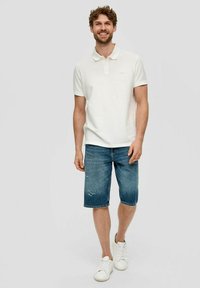 Weißes Poloshirt, Jeansshorts mit verwaschenen Details und weiße Sneakers. Lässiger Schnitt mit kurzen Ärmeln und Kragen.