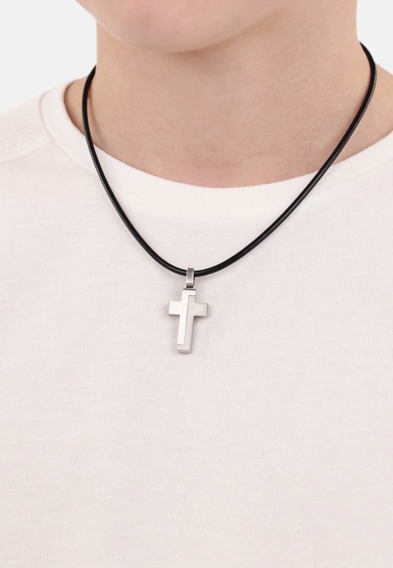 Silberner Metallkreuzanhänger an einem schwarzen Lederband, um den Hals getragen, über einem weißen strukturierten Hemd. Das Kreuz hat ein einfaches, modernes Design.