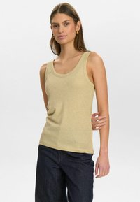 Light beige ribbed tank top with wide scoop neckline, fitted shape, soft texture, paired with dark denim jeans.