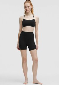 Schwarzes sportliches Crop-Top mit dünnen Trägern und hohen, schwarzen Shorts. Glatte Textur, figurbetontes Design, keine sichtbaren Muster oder Beschläge.