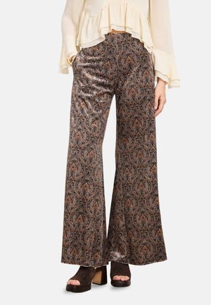 Pantalones de pierna ancha con un intrincado patrón de cachemira marrón y negro, combinados con zapatos negros de tacón bloque abiertos y una blusa crema con volantes.