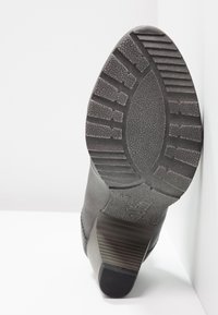 Semelle d'une botte noire à talon montrant un motif de bande de roulement texturé et un talon bloc empilé sur fond blanc.