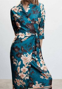 Bloemen jurk in teal satijn met lichtroze en zwarte bloemen, driekwart mouwen, een gestrikte taille en een vloeiende silhouet.