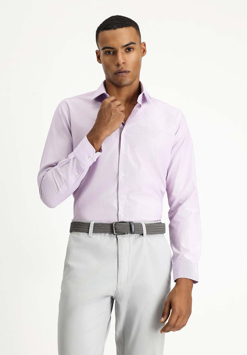 Camisa de vestir de color púrpura claro con un patrón texturizado, cuello hebilla, puños con botón y silueta ajustada, combinada con pantalones grises y cinturón trenzado.