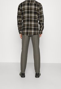 Camisa de franela a cuadros en negro y amarillo combinada con pantalones de espiga en gris. Presenta mangas largas y un diseño de botones, con zapatos negros.