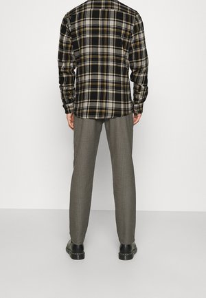 Chemise en flanelle à carreaux noir et jaune associée à un pantalon pied-de-coq gris. Comprend des manches longues et une conception à boutons, avec des chaussures noires.
