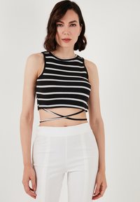 Čierny a biely pruhovaný crop top s okrúhlym výstrihom a krížovým dizajnom na chrbte. Tkanina vyzerá ako rebrovaná, v kombinácii s bielymi priliehavými nohavicami.