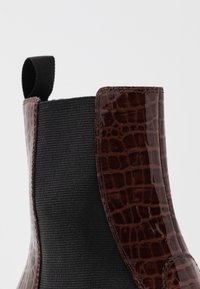Botín Chelsea de charol marrón con textura en relieve de cocodrilo, panel lateral elástico y tirador en la parte superior para facilitar su uso.