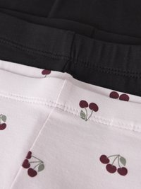 Κοντινή λήψη μαύρου και ανοιχτόροζ υφάσματος με κόκκινα τυπωμένα κεράσια και ορατές ραμμένες ραφές, που δείχνει την περιοχή της ζώνης ρούχου.