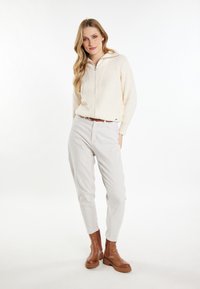 Maglione tricot crema con chiusura a zip, abbinato a pantaloni beige chiaro e stivaletti marroni con suola spessa.
