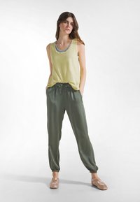 Jasnożółty, bezrękawnik z szerokim dekoltem, zestawiony z oliwkowozielonymi, luźnymi, mankietowanymi dresami oraz beżowymi, płaskimi butami.