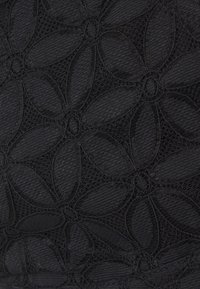 Tissu noir présentant un motif complexe de dentelle florale avec des pétales qui se chevauchent, des coutures soulignées et une surface texturée.