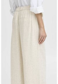 Pantaloni palazzo beige realizzati in un tessuto testurizzato, con vita elastica e una tasca sul retro per una funzionalità aggiuntiva.